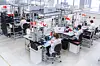 Laboratorielignende produksjonshall der teknikere monterer batteripakker ved arbeidsstasjoner.